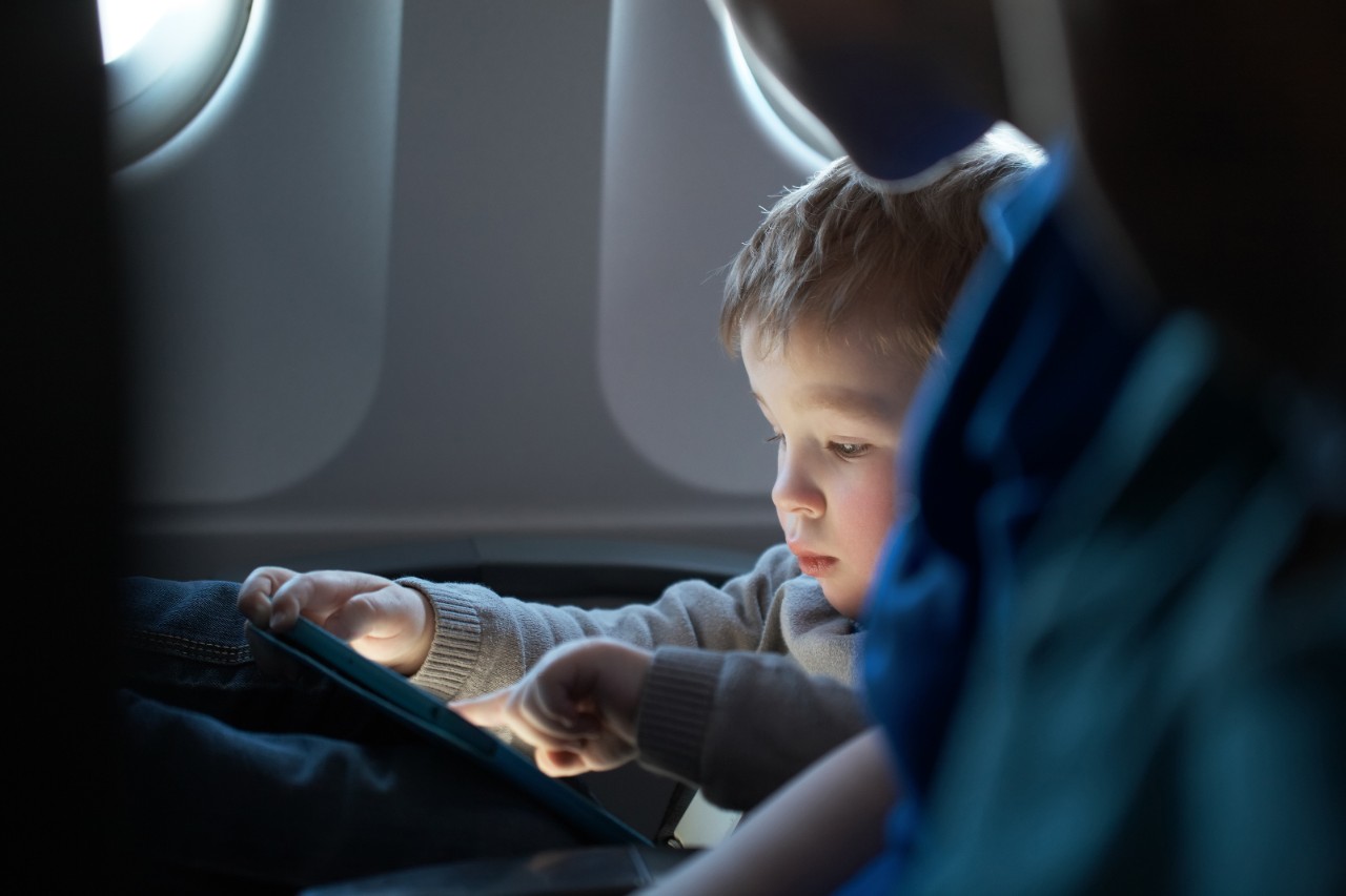 A toddler uses a tablet device in their airplane seat
